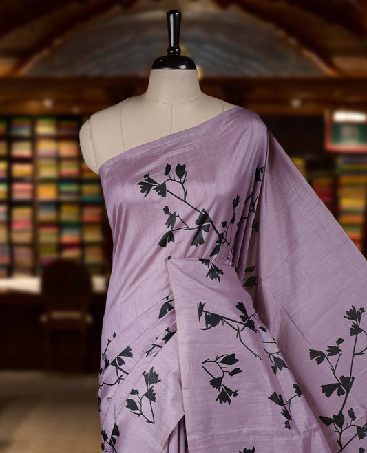 Pastel Lavender colour Semi tussar silk saree adorned with black floral prints on the body and an elegant pallu & Comes with a matching blouse piece for a classy look.