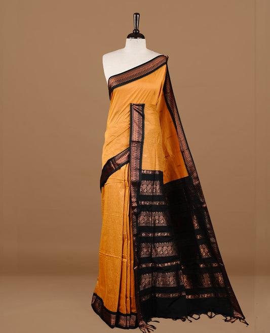 Mustard colour kalyani cotton saree featuring gold zari motifs on body, highlighting contrast Black colour with Antique gold zari border, paired with matching blouse piece.