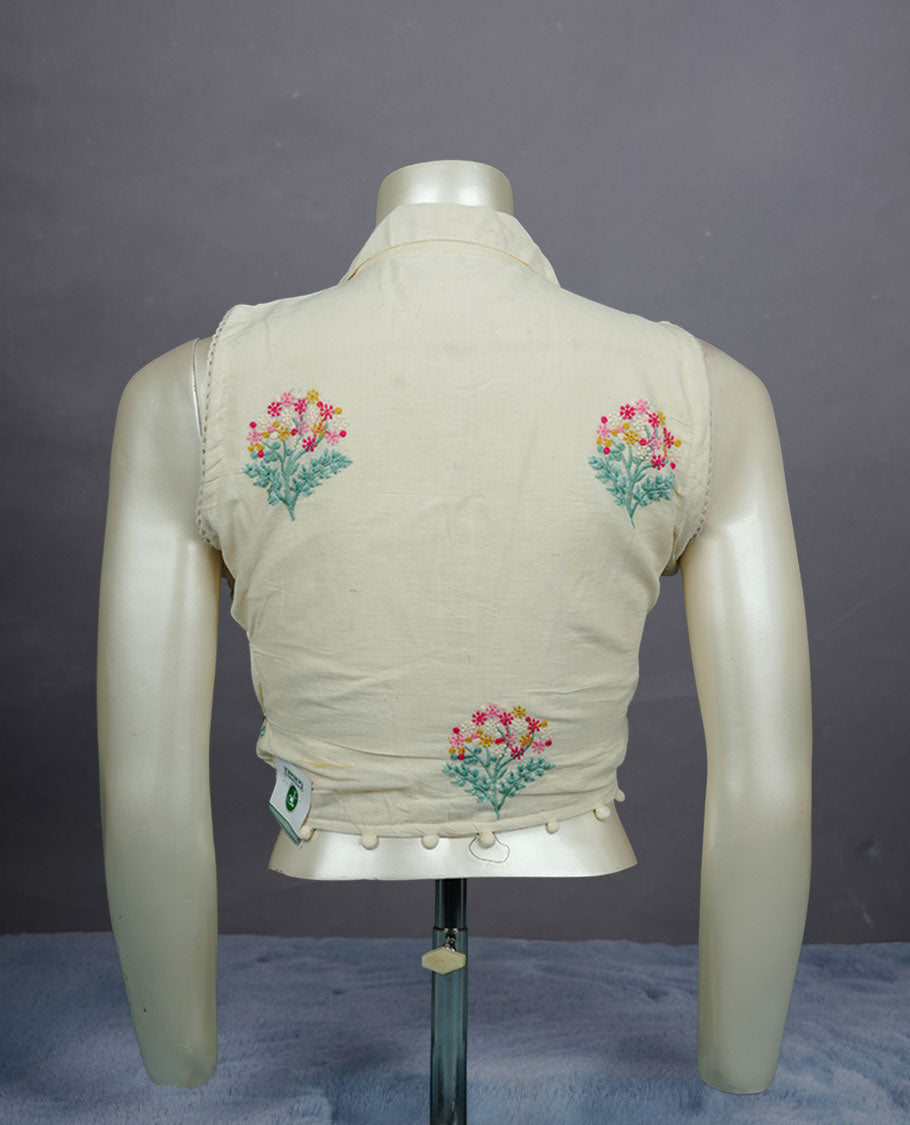 Ivory colour sleeveless cotton blouse with delicate floral embroidery, collared neckline, front button closure, and subtle pom-pom hem detailing for a soft ethnic touch.