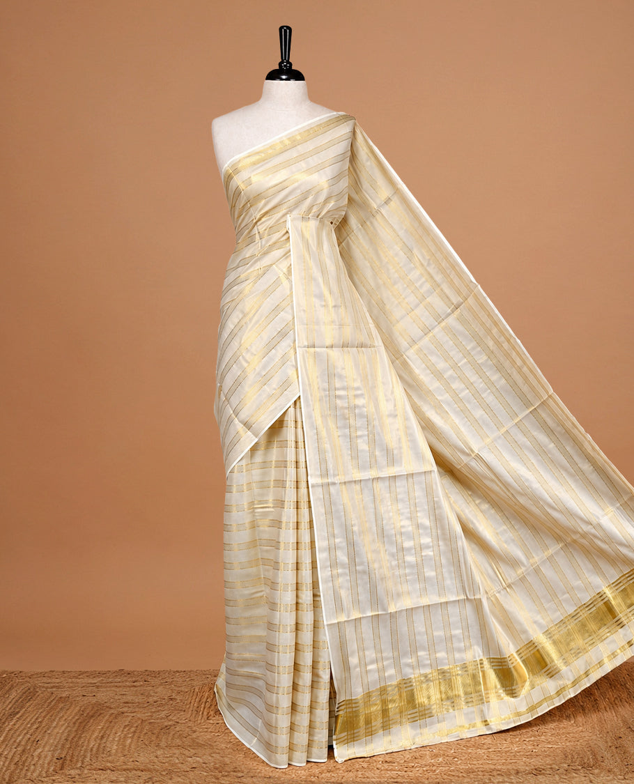 Cream Colour Tissue Kerala Saree Featuring Classy Gold zari stripes on Body, Enriched By Gold Zari Border, Paired With A Matching Blouse Piece.
