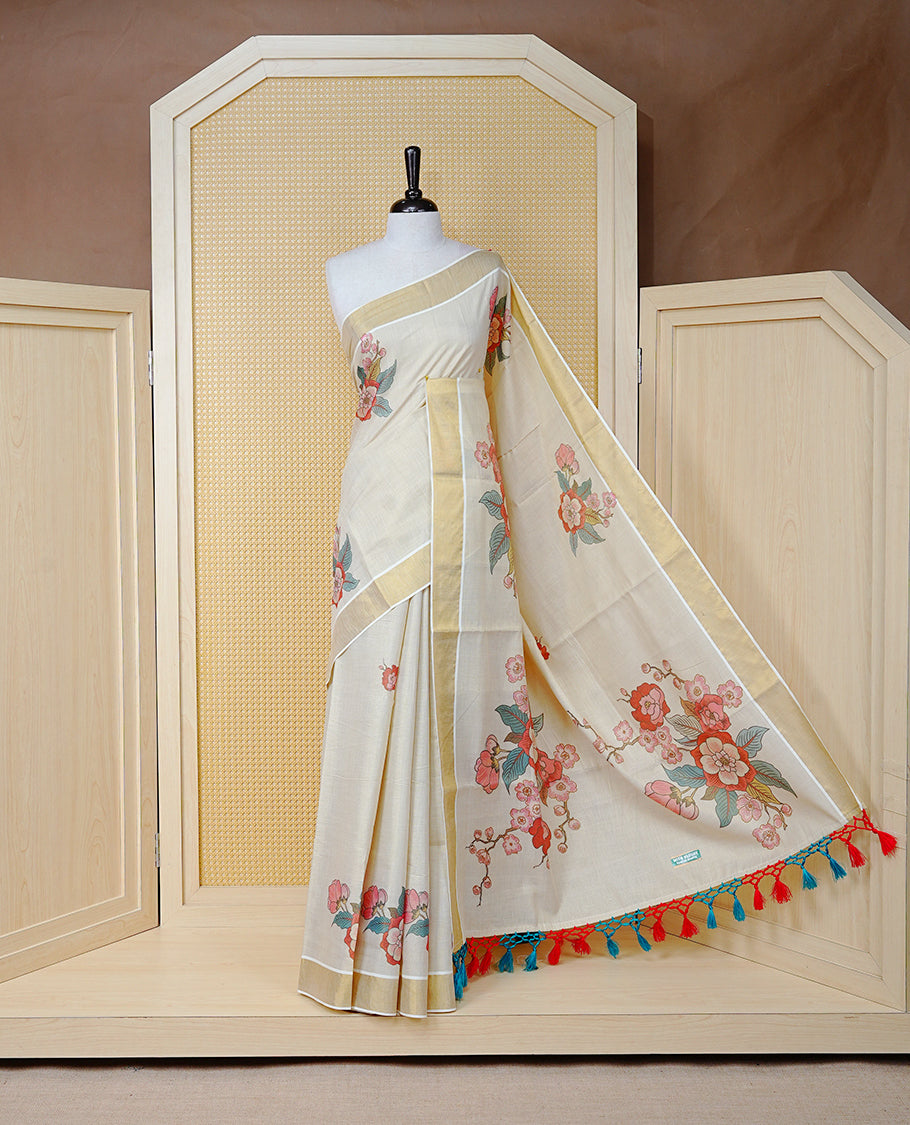 Cream Colour Tissue Kerala Saree Featuring Vibrant Digital Floral Prints Printed On Body & Pallu, Beautifully Enhanced With A Classic Gold Zari Border And Red & Blue  Tassels. Paired With A Matching Blouse Piece.
