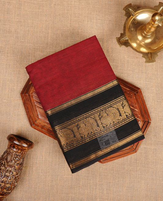 Dark red colour chettinad cotton saree featuring plain body, paired with a black colour traditional gold zari border paired with matching blouse.