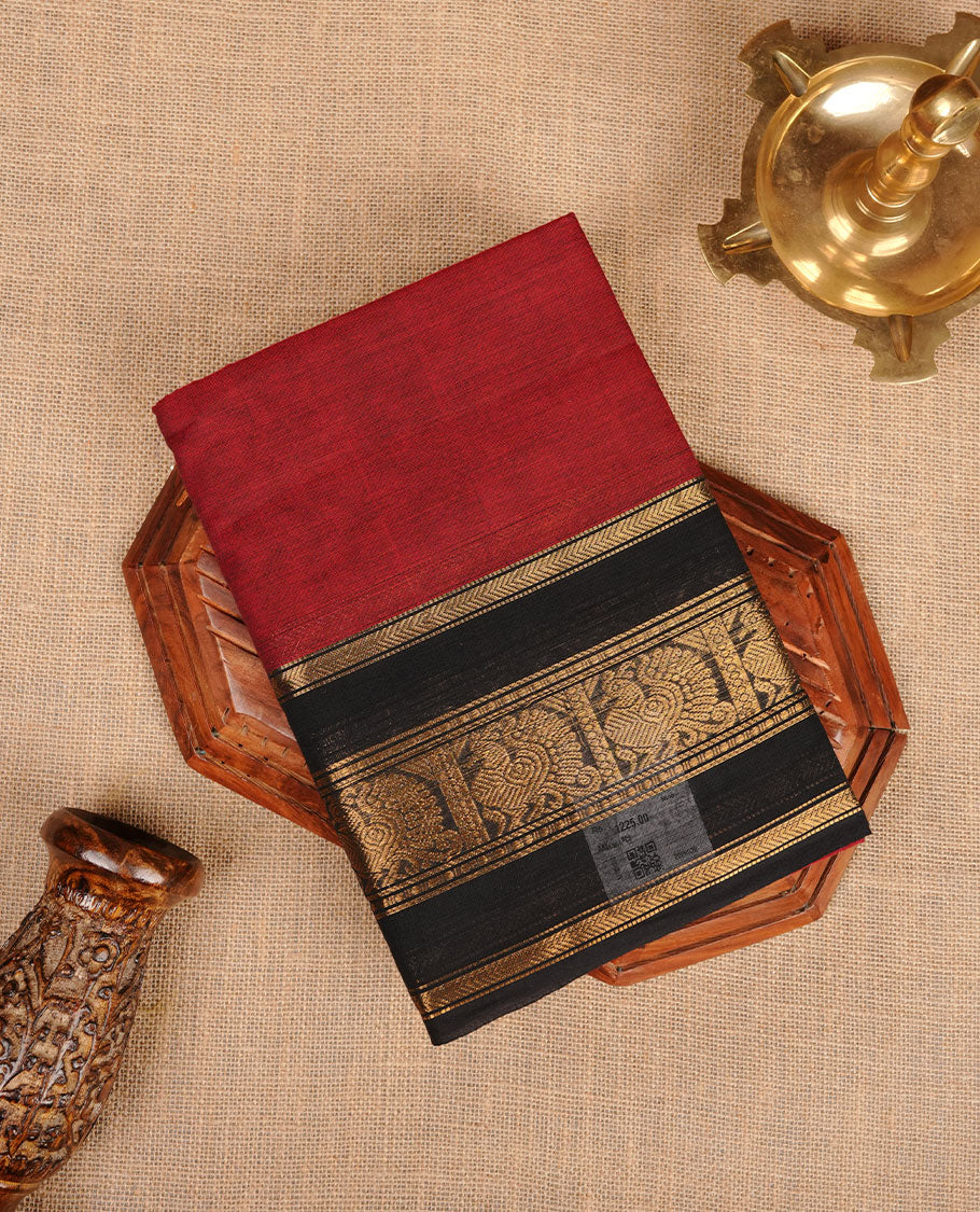 Dark red colour chettinad cotton saree featuring plain body, paired with a black colour traditional gold zari border paired with matching blouse.
