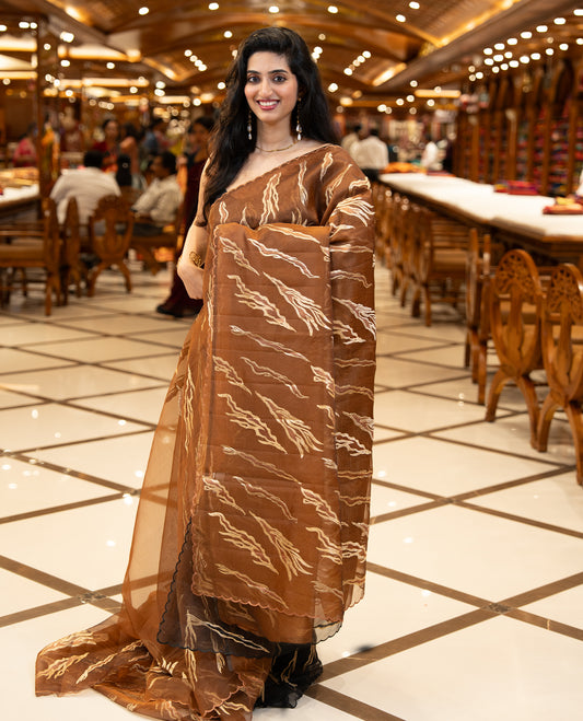 Brown colour sheer Organza saree featuring Gold thread embroidery with modern wavy & flame inspired motifs and scallop border, comes with matching organza blouse.