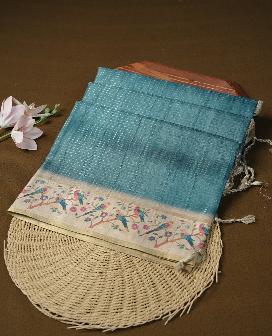 Teal colour tussar saree featuring golden zari dot stripped pattern on the body, complemented by a contrast cream colour mutlicolour floral kodi & animal print on border & pallu, paired with a matching blouse.