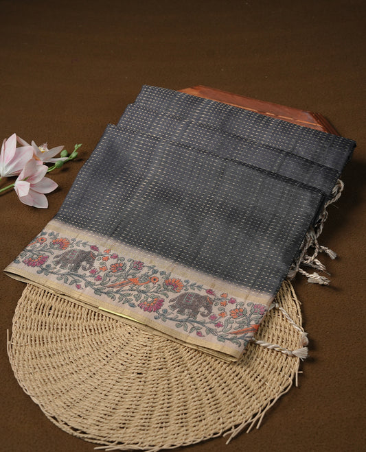 Charcoal black colour tussar saree featuring golden zari dot stripped pattern on the body, complemented by a contrast cream colour mutlicolour floral kodi & animal print on border & pallu, paired with a matching blouse.