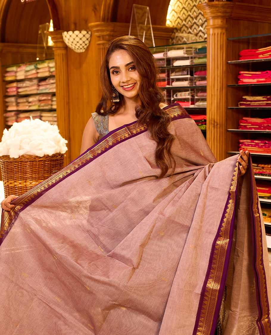 Muted rose pink colour chettinad cotton saree featuring subtle gold butta motifs on the body, highlighted with a rich purple contrast border and pallu accented in gold zari, paired with a matching blouse piece.