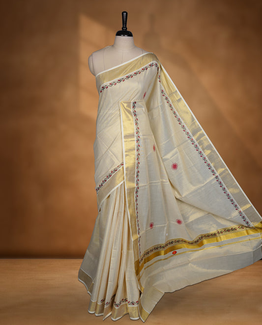 Off white colour Tissue Kerala saree featuring delicate floral border detailing, complemented by a classic golden zari border and traditional pallu, paired with a matching blouse.