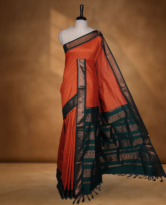 Rust orange colour Kalyani cotton saree featuring a plain elegant body, complemented by a rich dark green zari border and traditional woven pallu, paired with a matching blouse.