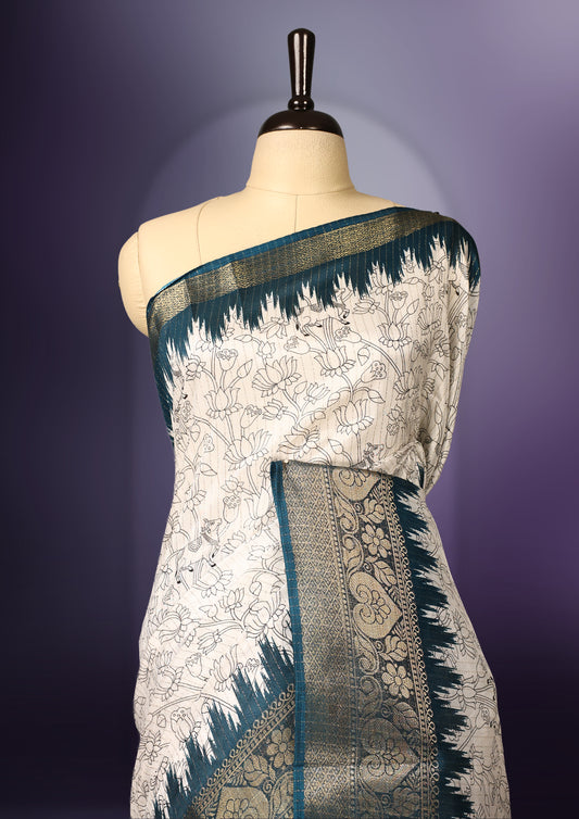 White colour saree adorned with delicate floral designs across the body, enhanced by a rich teal and gold zari border, featuring a vibrant artistic pallu with tree and animal motifs, paired with a matching blouse.