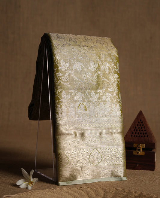 Light olive-gold antique zari tissue brocade saree with delicate woven floral motifs, a traditional gold zari border and pallu, paired with a matching blouse.
