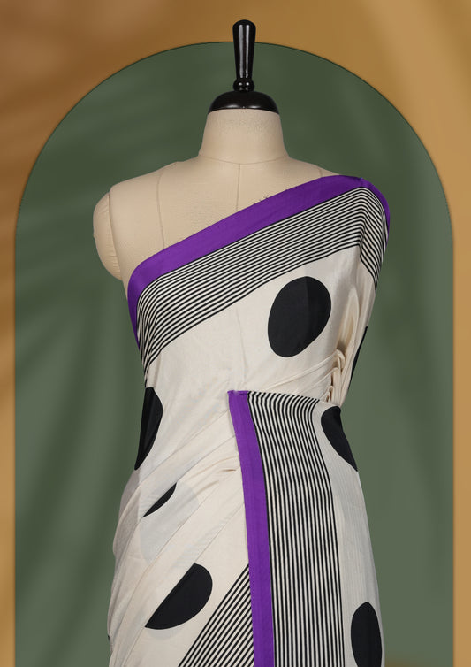 Cream colour saree with bold black polka dots and striped patterns, highlighted by a vibrant purple border & Comes with a stylish matching blouse.
