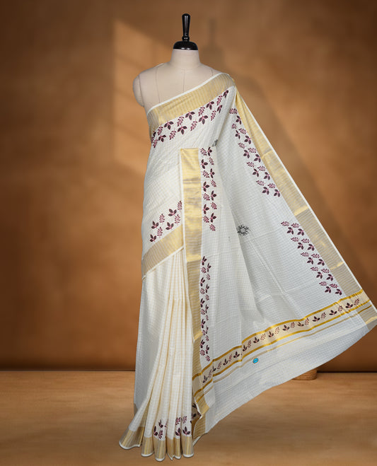 Off white colour cotton Kerala saree featuring a gold zari check pattern across body, a refined kasavu border with leaf print, paired with a matching blouse.