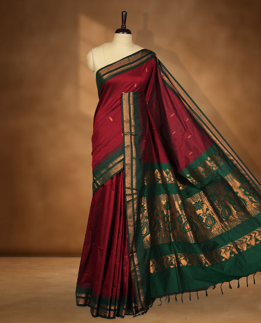 Maroon colour kalyani cotton saree featuring Antique zari motifs on body, contrast green colour border with geometric antique zari pattern, paired with matching blouse piece.