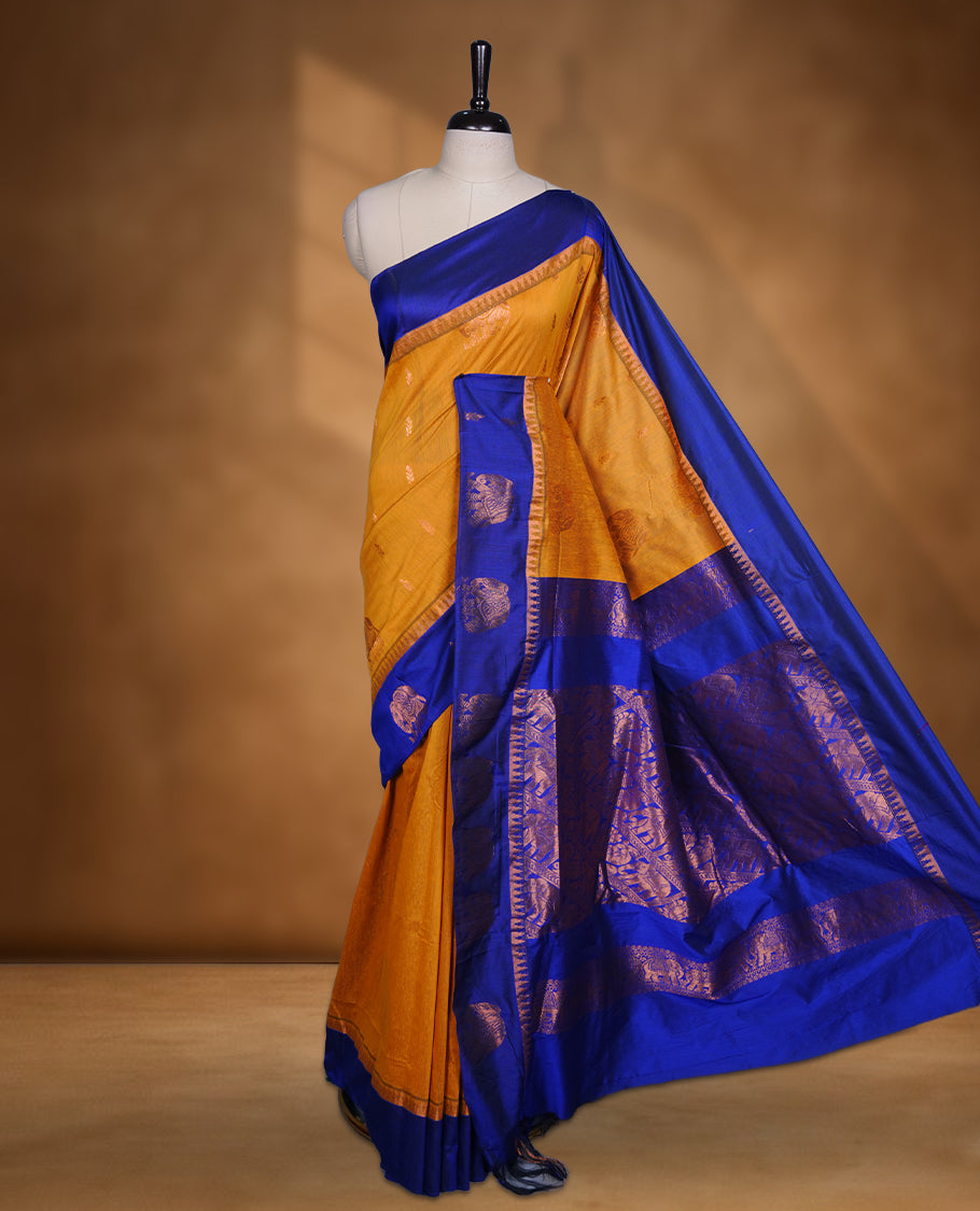 Mustard colour mixed Kalyani cotton saree with subtle zari motifs, royal blue zari border and elephant motif pallu, paired with a matching blouse.