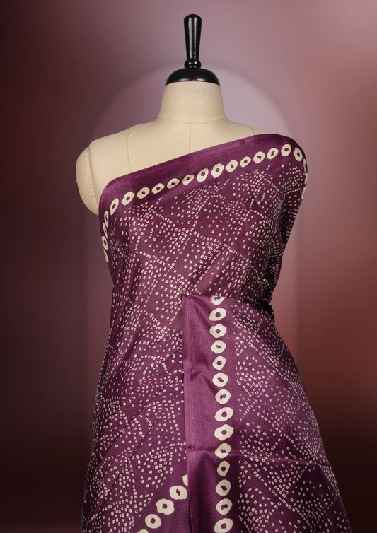 Dark grape colour saree adorned with intricate beige bandhani patterns and a contrasting pallu featuring exquisite beige floral motifs, perfectly paired with a matching blouse for a regal look.