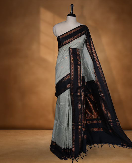 Grey colour Kalyani cotton saree featuring a plain elegant body, complemented by a black zari border and traditional woven pallu, paired with a matching blouse.