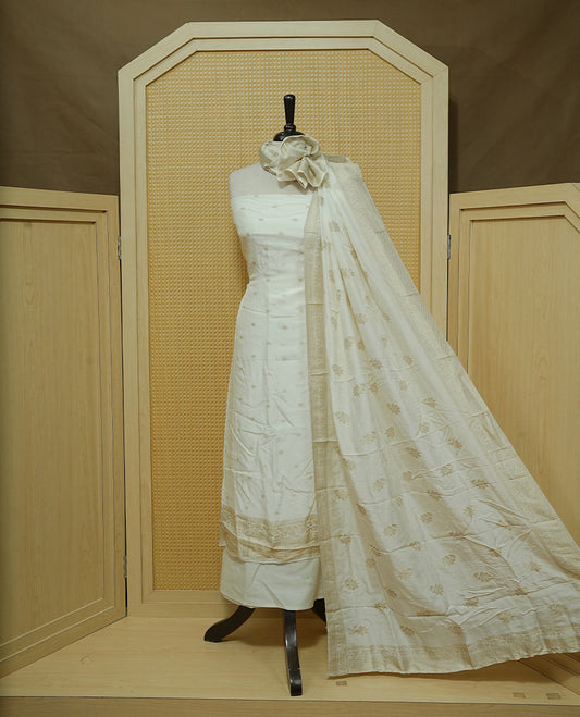 Cream colour Salwar material featuring gold zari Buttas on body, paired with matching dupatta & Bottom.