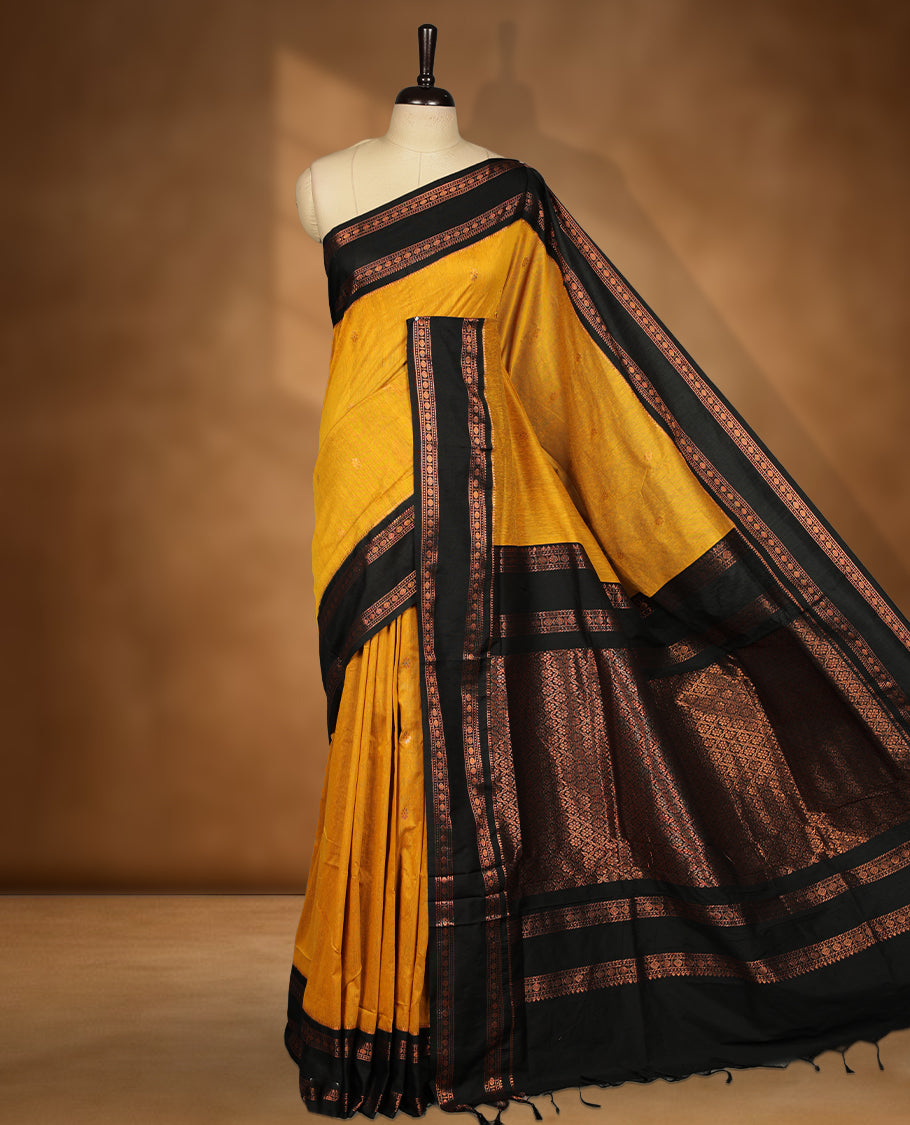 Mustard colour kalyani cotton saree featuring Antique zari motifs on body, contrast Black colour border with floral and chakra antique zari pattern, paired with matching blouse piece.