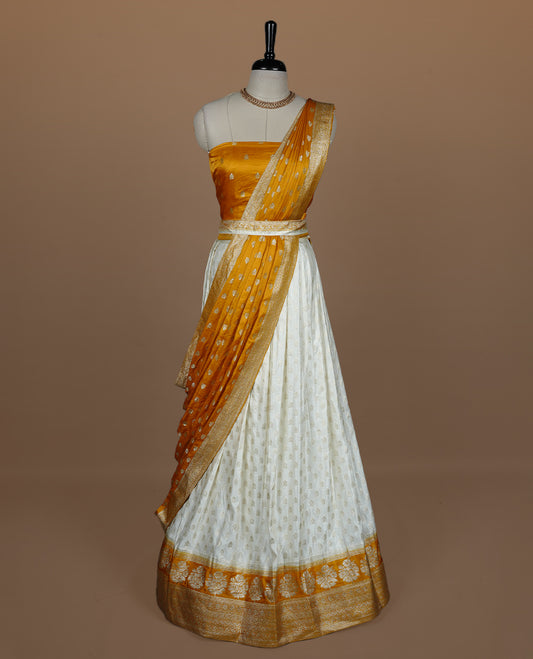 Off white semi banaras semi stitched dhavani set featuring gold zari motifs and contrast Yellow colour and traditional border, unstitched gold zari blouse piece and matching Duptta.