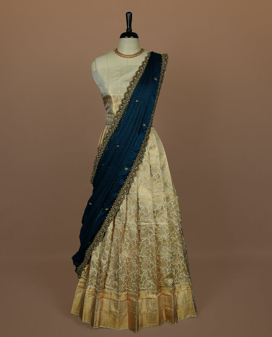 Light gold colour semi banaras semi stitched dhavani set featuring gold zari floral kodi motifs and traditional border, unstitched matching blouse piece and contrast Teal colour Duptta with gold thread and beats worked border.