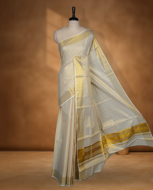 Off white colour Tissue Kerala saree featuring a subtle checked body, a refined golden zari border, and a traditionally woven pallu, paired with a matching blouse.