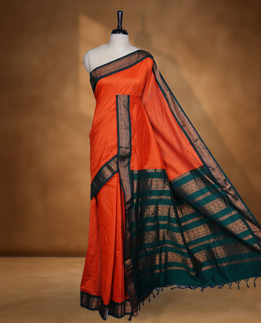 Rust orange colour Kalyani cotton saree featuring a plain elegant body, complemented by a rich green zari border and traditional woven pallu, paired with a matching blouse.