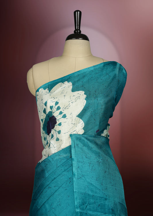 Teal blue colour saree with bold white floral motifs and subtle navy blue accents, exuding timeless elegance and modern charm, paired with a matching blouse.