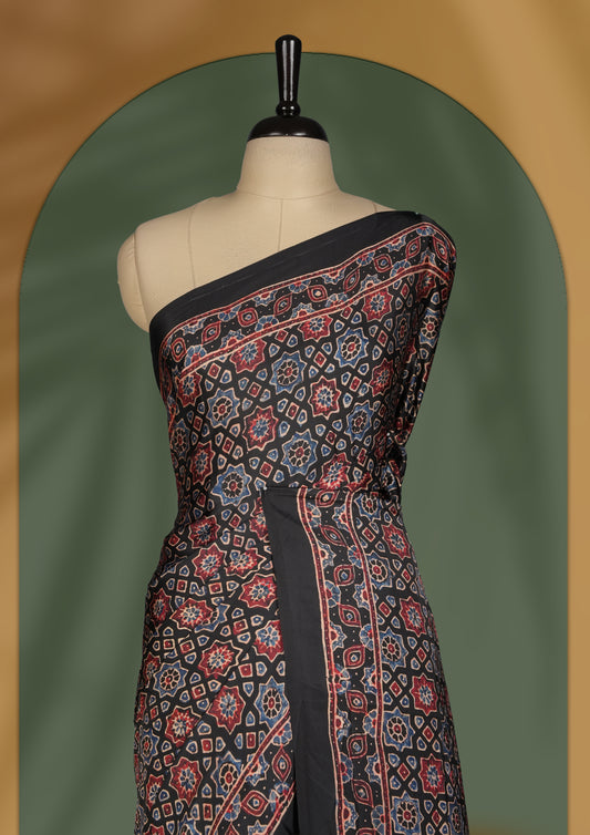 Black colour saree featuring intricate traditional prints in earthy tones, finished with a sleek satin border and tassel details & Comes with a stylish matching blouse.