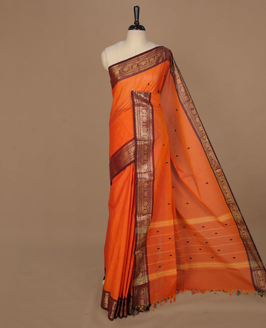 Orange colour chettinad cotton featuring black thread motifs on body, complemented by contrast brown colour with gold zari border, paired with matching blouse piece.