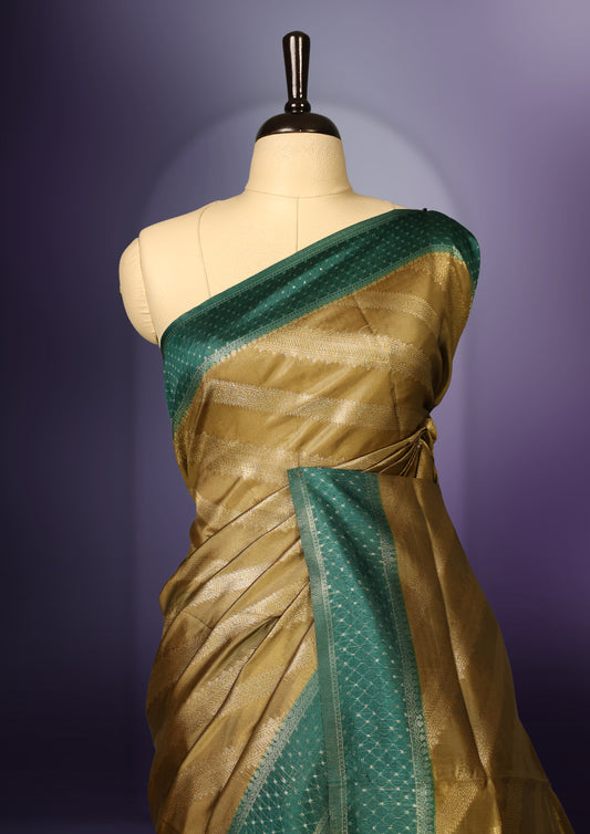 Golden saree featuring subtle self striped woven patterns on the body, enhanced with a green geometric border, complemented by a rich zari pallu with tassels, and paired with a matching blouse for a traditional elegant look.