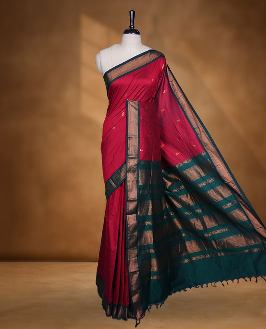Dark maroon colour Kalyani cotton saree featuring delicate zari buttas on the body, complemented by a dark green zari border and woven pallu, paired with a matching blouse.