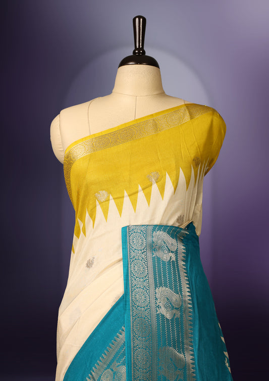 Off white and yellow colour saree adorned with subtle woven motifs across the body, enhanced by a rich teal and silver zari border, featuring a vibrant artistic pallu with intricate traditional patterns, paired with a matching blouse.