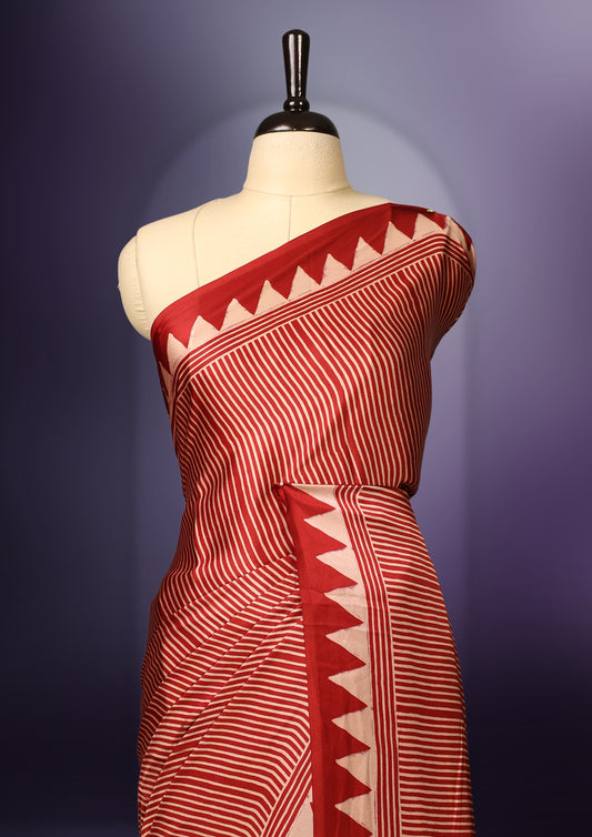 Maroon colour saree featuring bold striped patterns across the body, accentuated with a striking triangular border, and a contrasting pallu with geometric detailing, paired with a matching blouse