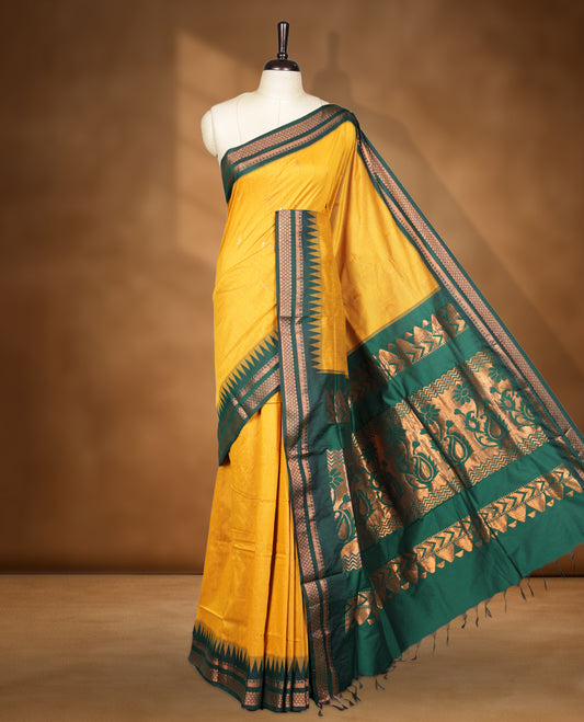 Mustard colour kalyani cotton saree featuring Antique zari motifs on body, contrast green colour border with geometric antique zari pattern, paired with matching blouse piece.