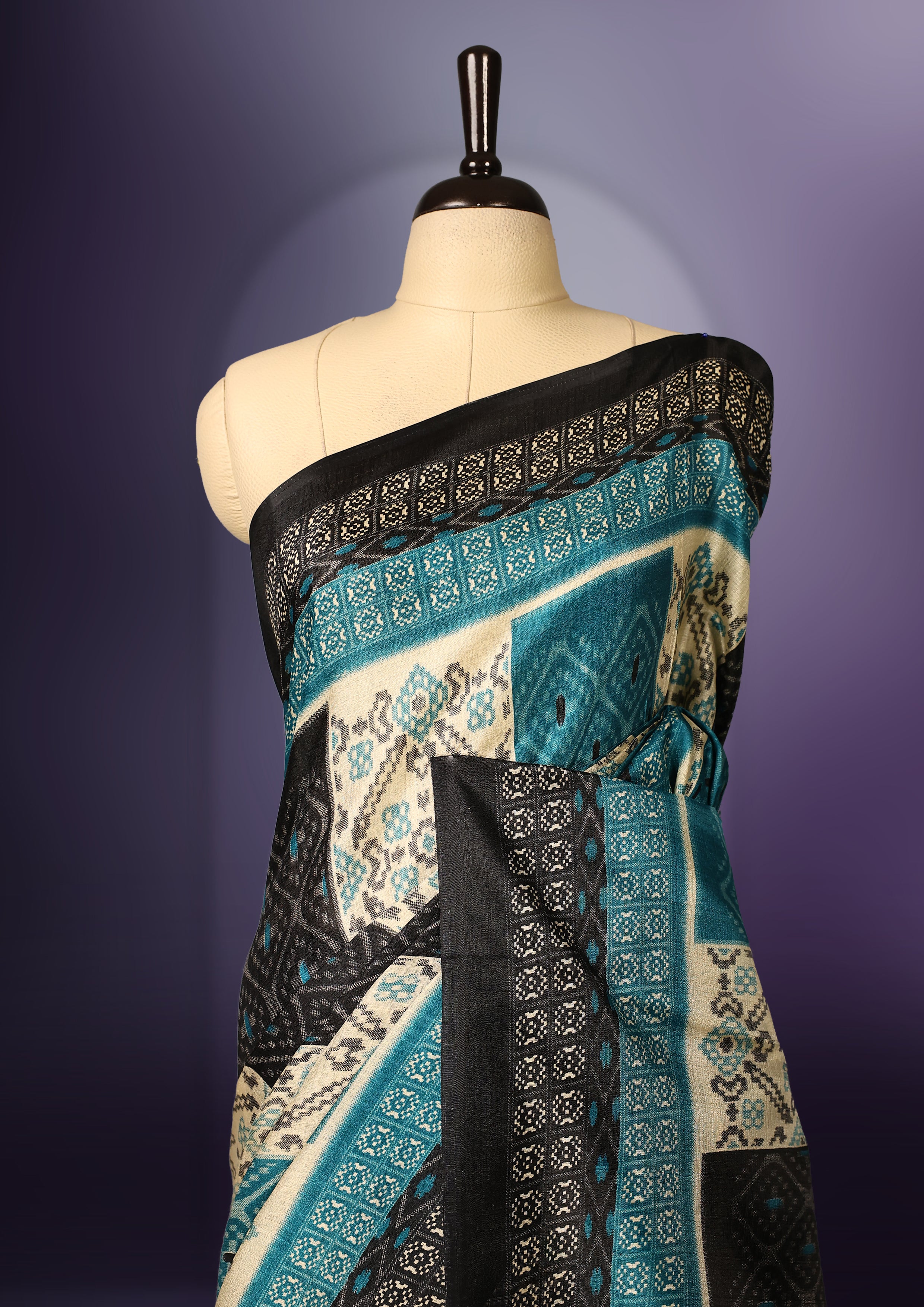 Charming teal, black, and cream printed saree featuring intricate geometric and floral designs, accentuated with a bold black border and tassel finish & paired with a matching blouse.