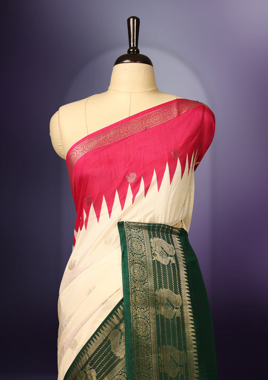 Off white colour saree with subtle golden buttas, highlighted by a vibrant pink pallu and rich green zari border adorned with intricate motifs, paired with a matching blouse.