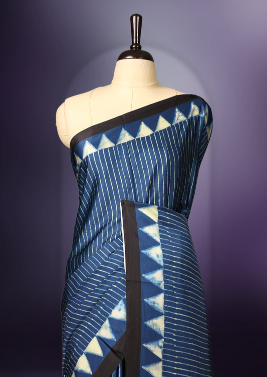 Blue colour saree featuring fine striped patterns across the body, accentuated with bold triangular designs along the border, and a contemporary pallu with geometric detailing, paired with a matching blouse.
