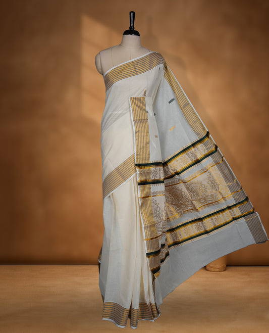 Off white cotton Kerala saree with a plain body and subtle motifs, striped golden zari border, and rich traditional pallu with green accents, paired with a matching blouse.