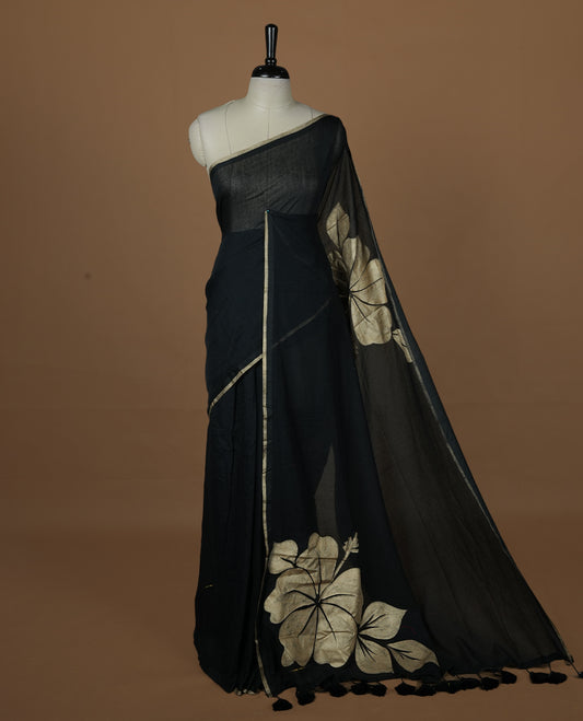Black coloured mul cotton saree featuring bold gold-tone floral motifs across the body, designed without a border and comes without a blouse piece.