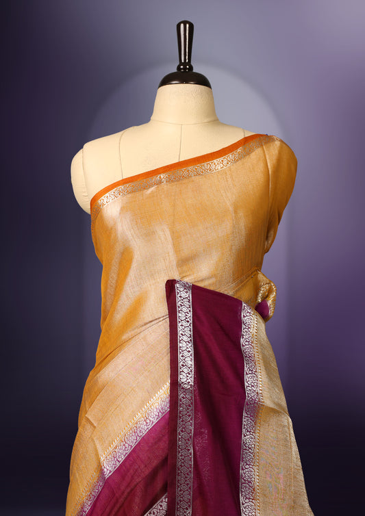 Golden yellow saree with a rich maroon border and pallu, accentuated by delicate silver zari detailing and tassel finish & The fabric has a lustrous sheen and comes with a matching blouse piece.