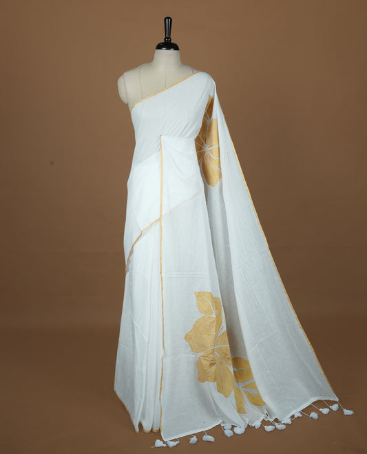 White coloured mul cotton saree featuring bold gold-tone floral motifs across the body, designed without a border and comes without a blouse piece.