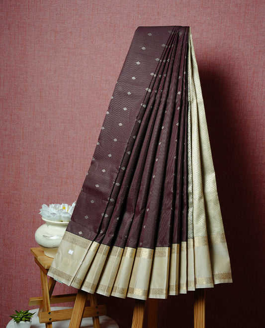 Chocolate brown coloured soft silk saree featuring gold zari stripes and motifs across the body, enhanced with a contrast Cream border and pallu, paired with a matching contrast blouse piece.