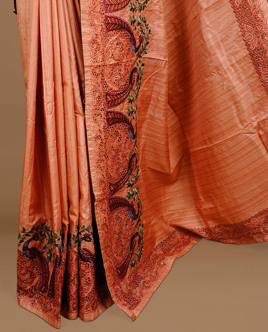 Peach colour Semi Tussar silk saree features an intricate cutwork embroidered peacock motifs on border, paired with a matching unstitched blouse piece.