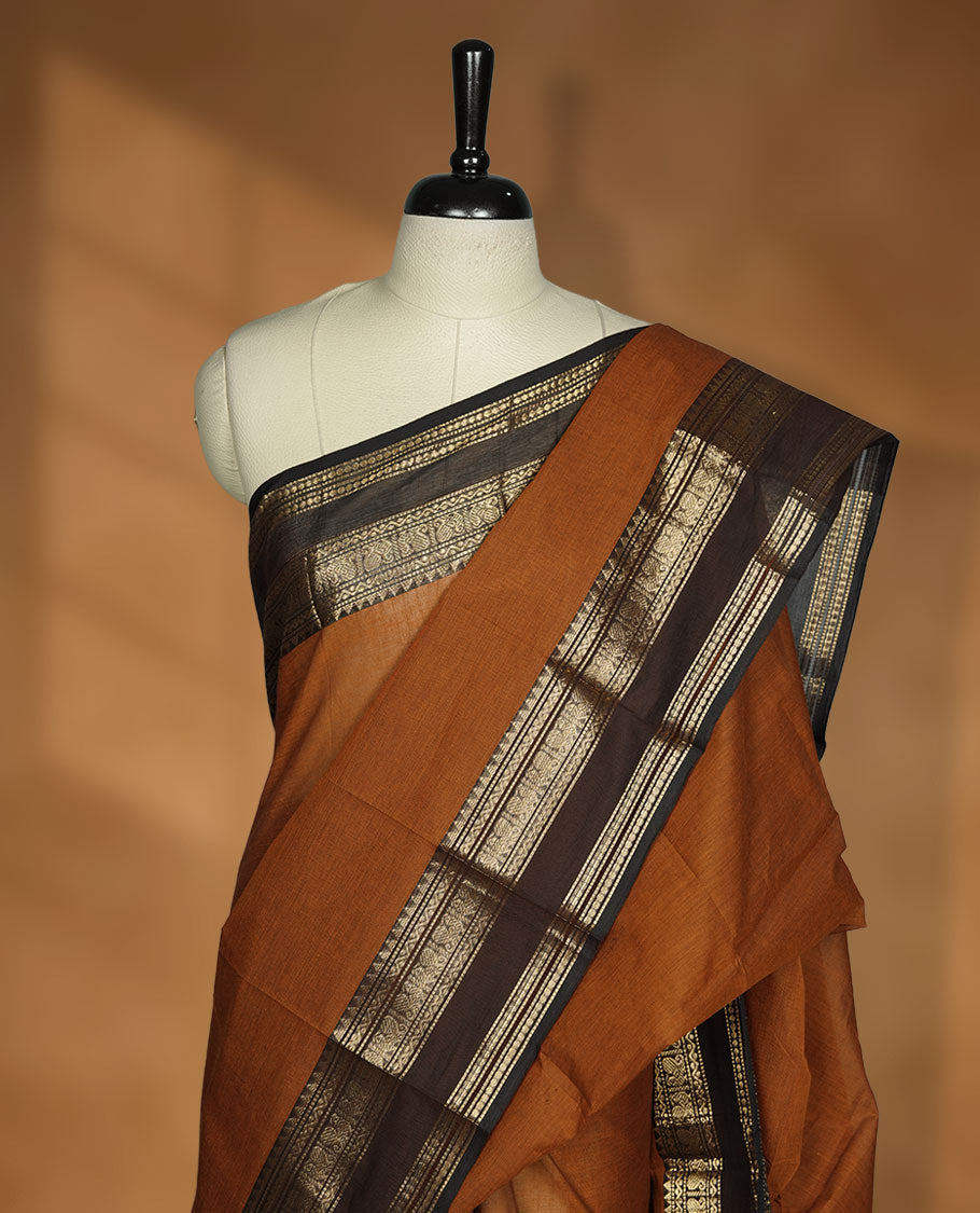 Burnt orange colour chettinad cotton saree featuring plain body, contrast Chocolate brown colour with traditional gold zari border paired with matching blouse.