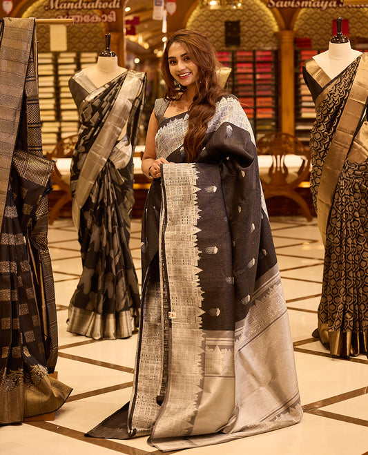 Charcoal black pure Kancheepuram silk saree with silver zari buttis, featuring a London architecture inspired silver zari pallu, a broad silver zari border, and a matching blouse