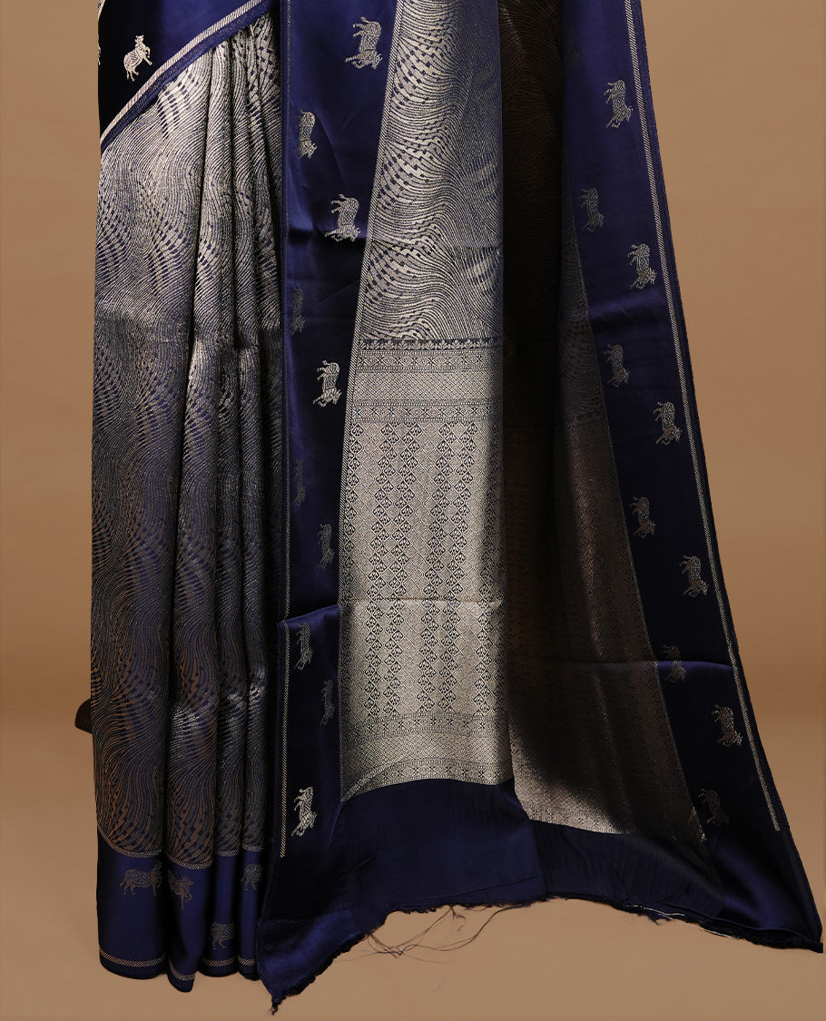 Dark Blue colour semi Banaras crepe silk saree featuring an elegant gold zari patterned body, highlighted by a plain border adorned with traditional gold zari cow motifs. Paired with a matching blouse piece.