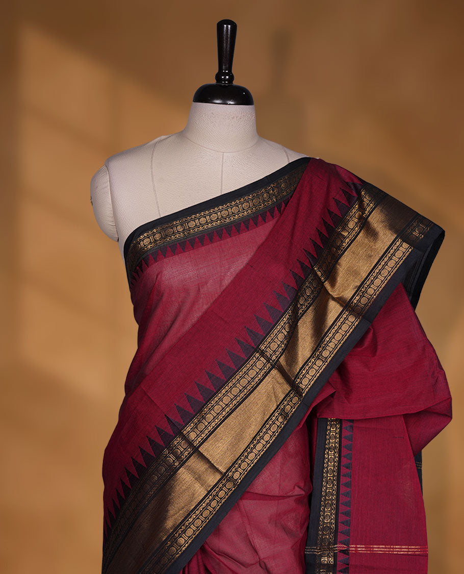 Deep red colour chettinad cotton saree featuring elegant plain body highlighting contrast black colour with gold zari traditional border, pallu and paired with matching blouse piece.