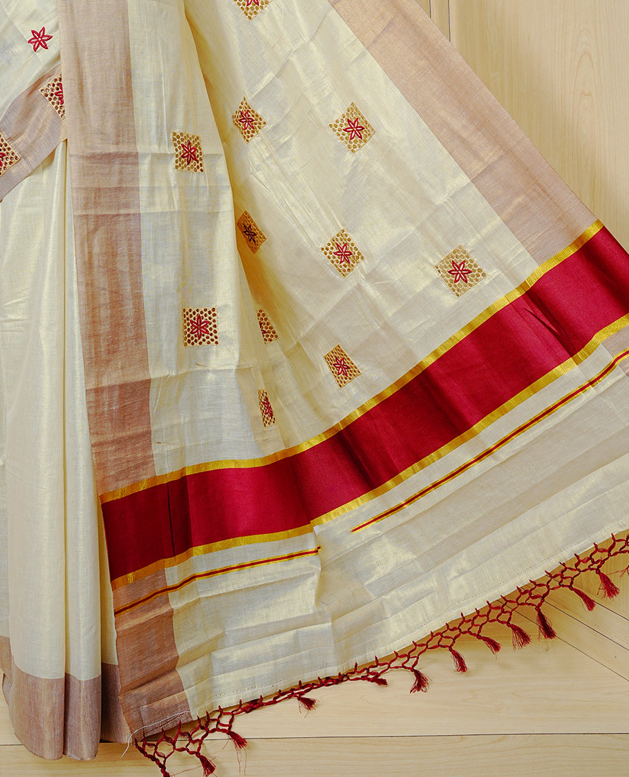 Cream Colour Tissue Kerala Saree Featuring Delicate Brick Red Floral Embroidery Work Across The Body, Enhanced With A Light Brown Zari Border And A Rich Brick Red & Gold Zari Pallu, Finished With Brick Red Tassels And A Matching Blouse Piece