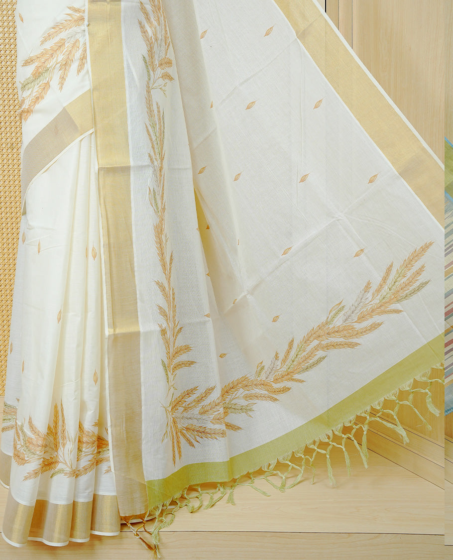 Cream Colour Cotton Kerala Saree Featuring Delicate Wheat Motifs and Scattered Leaf Designs On Body, Enhanced with a Classic Gold Zari Border. The Pallu Is Finished with Light Green Tassels and Paired with a Matching Blouse Piece.